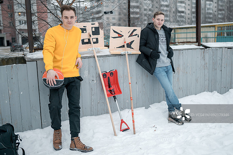 两位年轻男人在冬季篮球场上拿着雪铲摆姿势图片素材