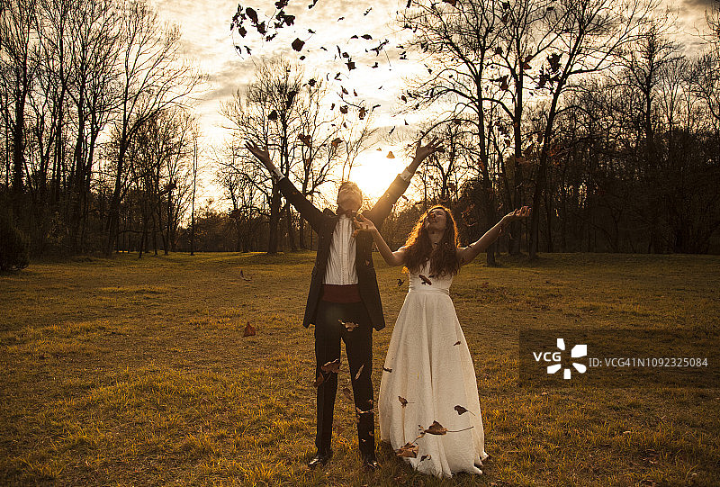 在公园里欢呼雀跃并抛洒树叶的幸福新婚夫妇图片素材