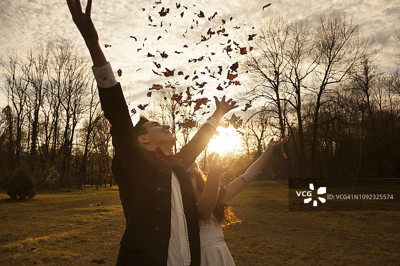 在公园里欢呼雀跃并抛洒树叶的幸福新婚夫妇图片素材