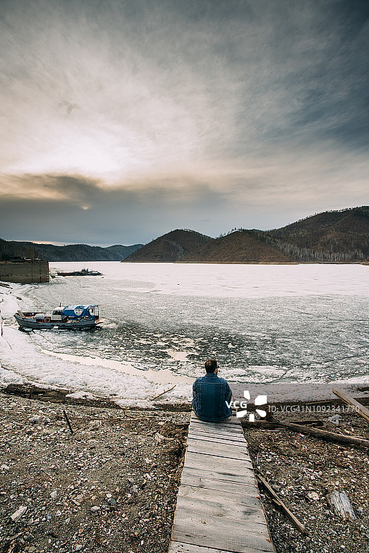俄罗斯阿穆尔州，坐在木板路上的男人看着风景的背影图片素材