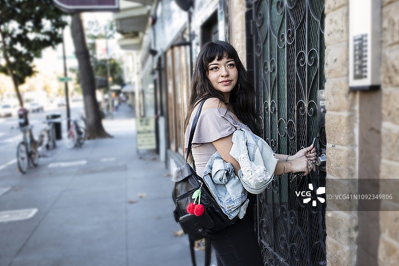 拉丁裔年轻女子在繁忙的城市街道上打开公寓门锁图片素材