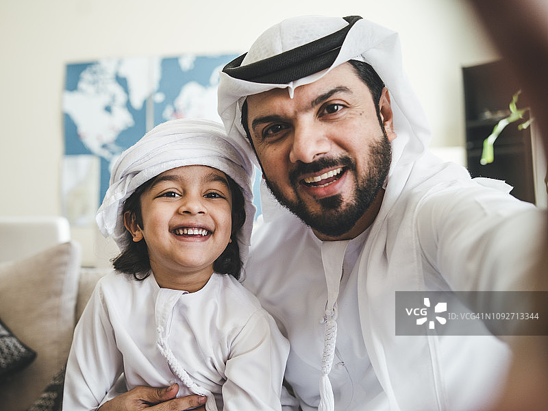 阿拉伯男人在家中沙发上与儿子自拍图片素材