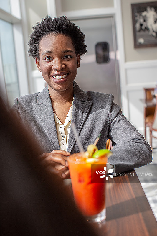 在机场酒吧，非裔美国女商人和同事喝着血腥玛丽，笑容满面图片素材