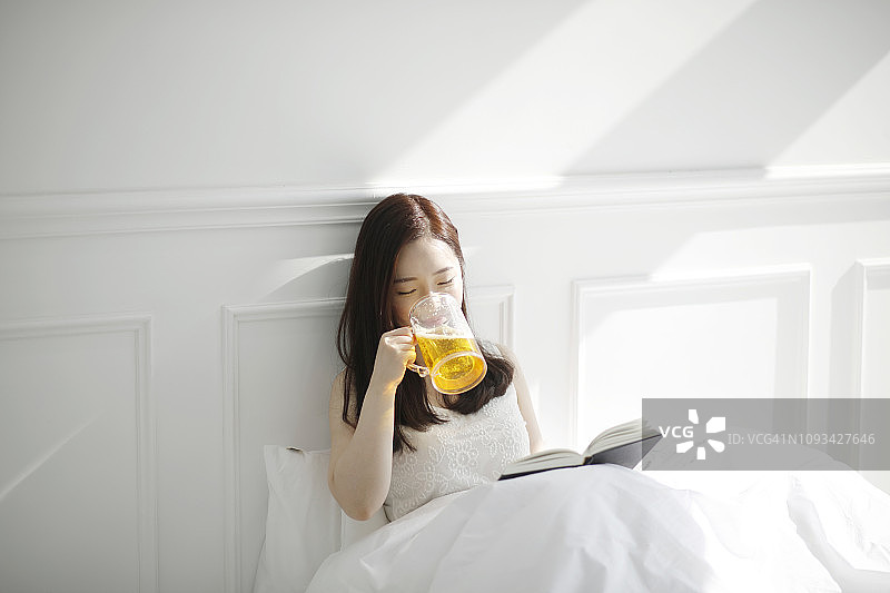 年轻女人在床上喝啤酒图片素材