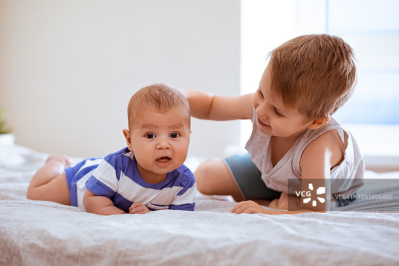 可爱的男孩和婴儿在卧室里放松玩耍。小弟弟拥抱她的新生婴儿。幼儿与新兄弟姐妹见面。图片素材