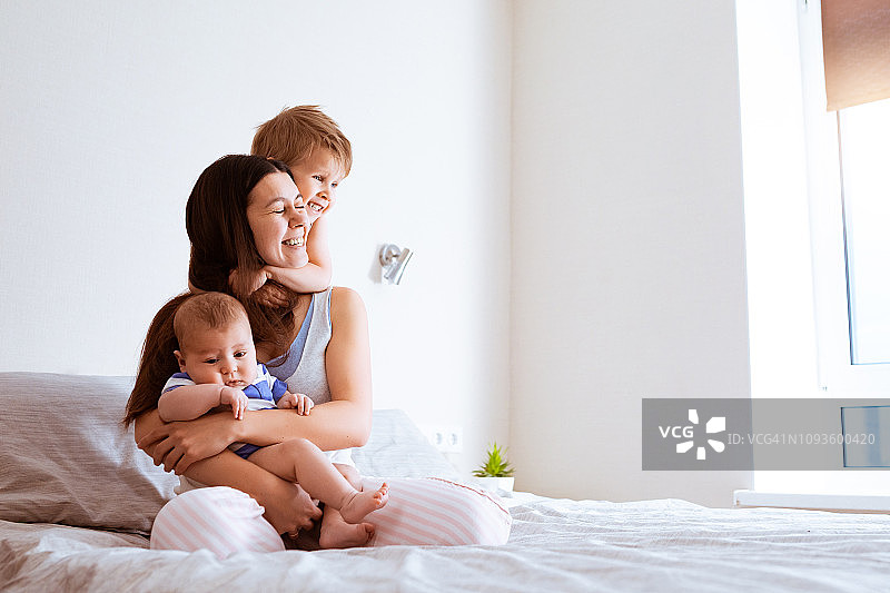 幸福的母亲和两个儿子，年轻的妈妈在晚上放松地拥抱她的孩子们图片素材