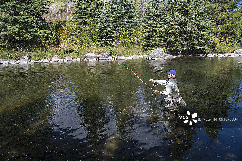 在科罗拉多落基山脉的蓝色河流里飞钓的年长妇女图片素材