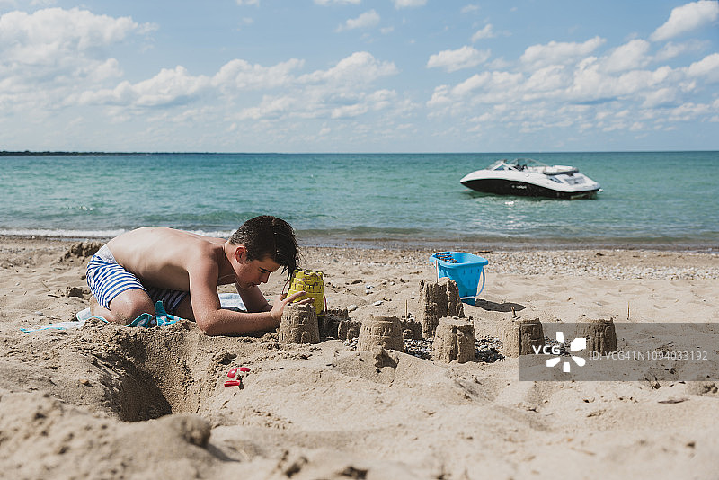 在阳光明媚的海滩上堆沙堡的赤膊男孩图片素材