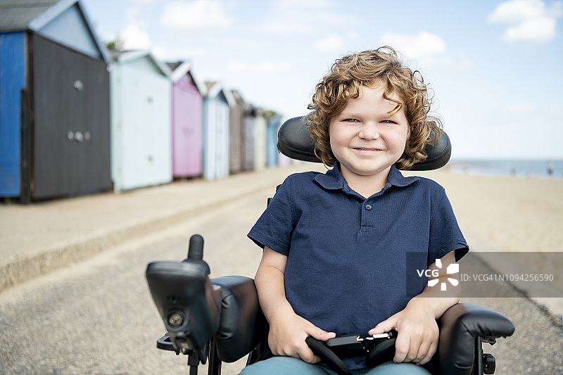 坐在轮椅上的残疾男孩在海滩小屋旁图片素材