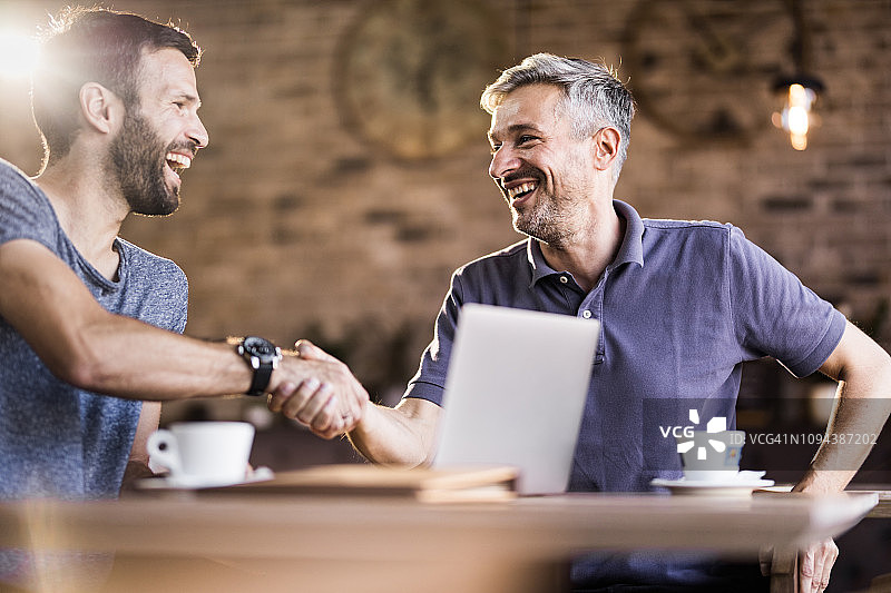 快乐的中年男人在咖啡馆里握手图片素材