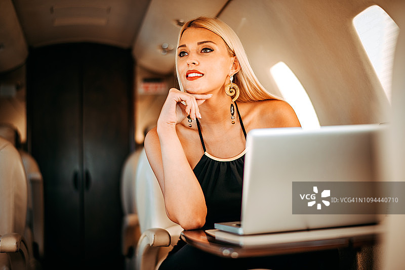 在私人飞机上使用笔记本电脑工作的漂亮金发女经理图片素材