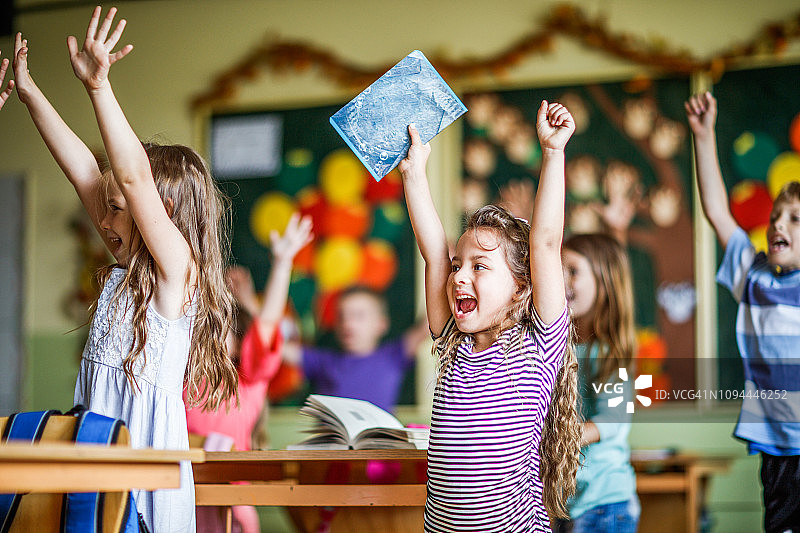 一群快乐的小学生在教室里举起手臂图片素材