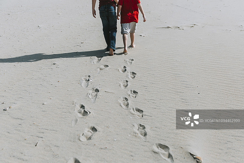 阳光明媚的日子里，兄弟俩在沙滩上行走图片素材