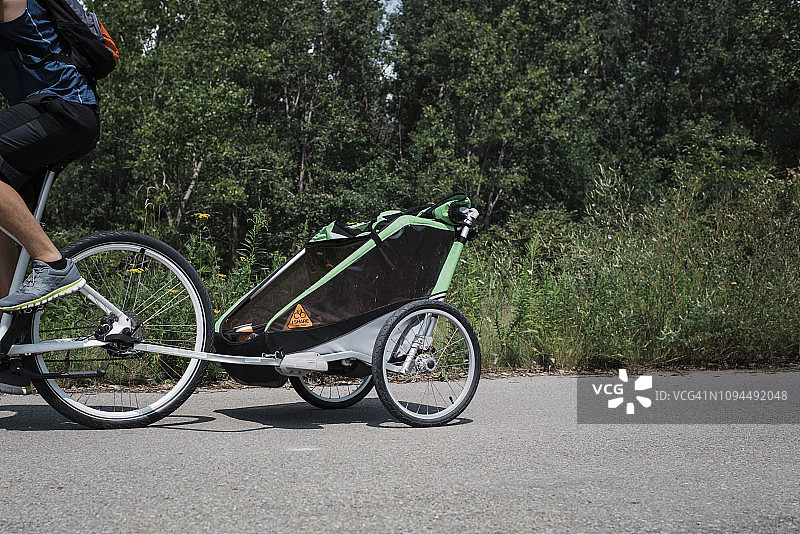 阳光明媚的日子里，男人骑着带拖车的自行车在树木间的道路上行驶图片素材