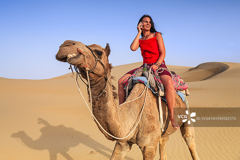 年轻女游客在印度拉贾斯坦邦骑骆驼使用手机图片素材