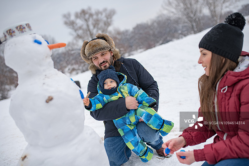 年轻父母和儿子一起堆雪人图片素材
