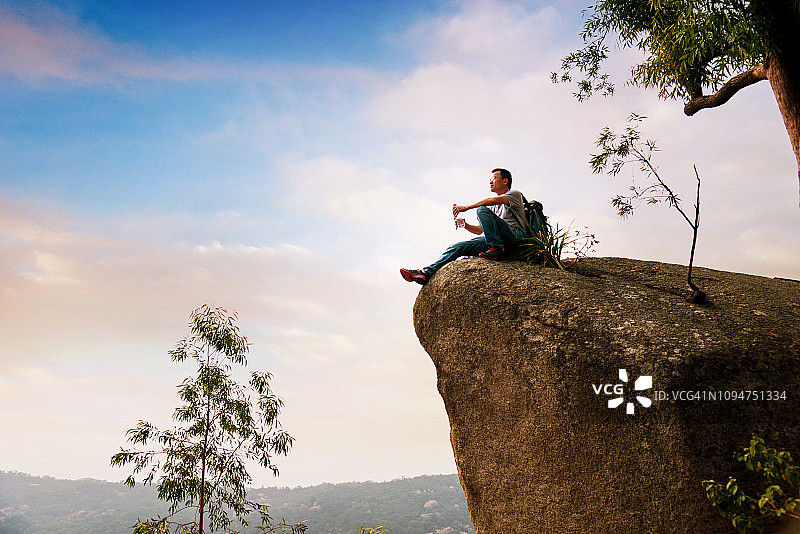 坐在岩石上喝水的徒步男子图片素材
