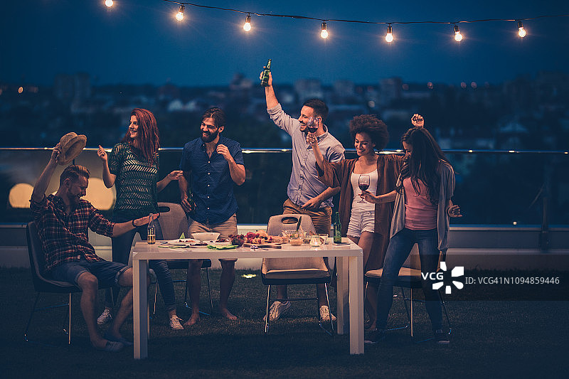 年轻快乐的人们在顶楼阳台上举行晚会。图片素材