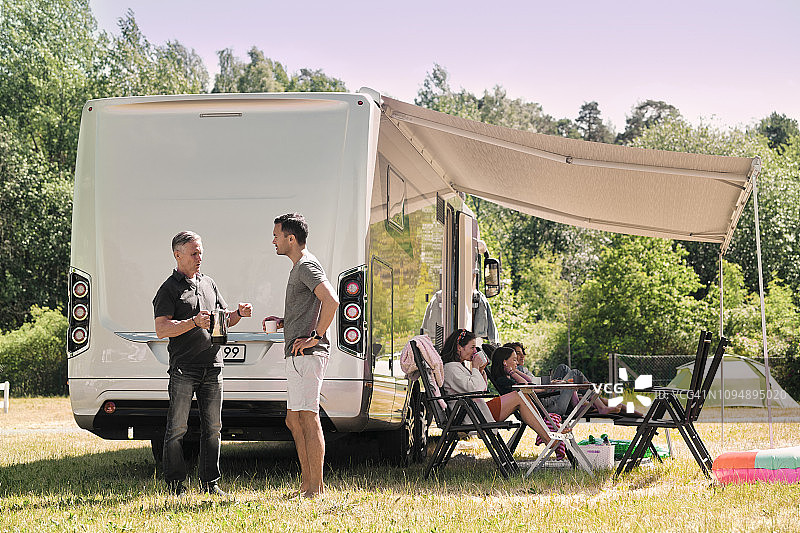 老年男人在露营地与家人在面包车外放松时与儿子交谈图片素材