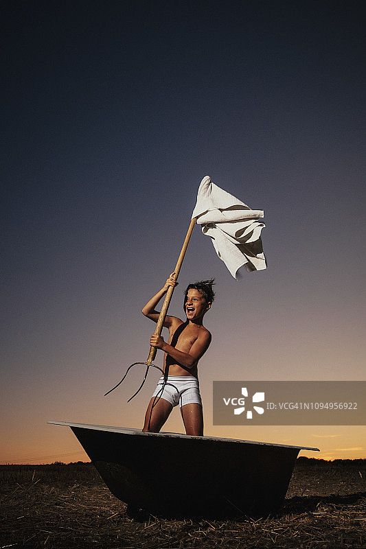 在乡村田野浴缸里挥舞草叉和白旗的顽皮男孩图片素材