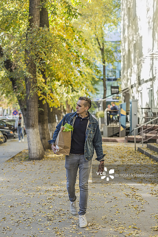 男人在秋天的 sidewalk 上提着食品杂货图片素材