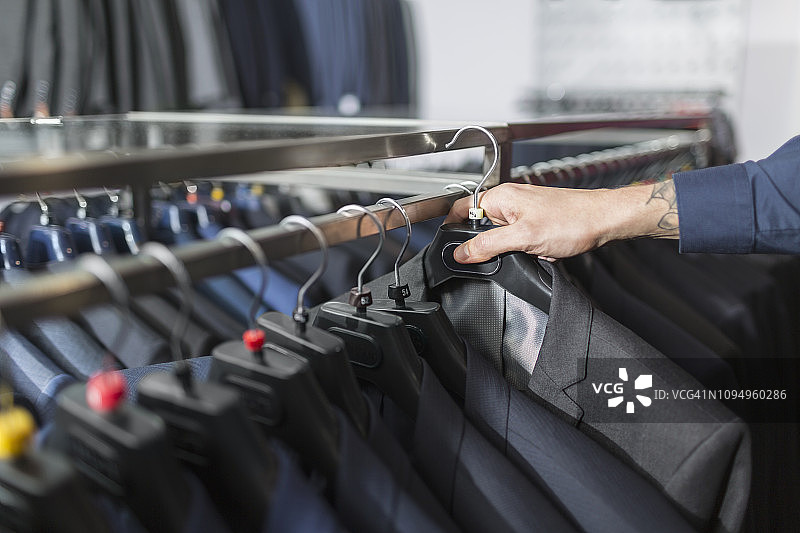 男人在男装店伸手去拿衣架上的西装图片素材
