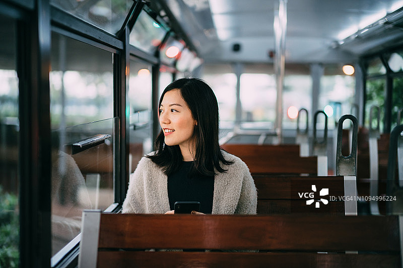 在城市电车上，年轻女人正在看窗外并使用手机图片素材