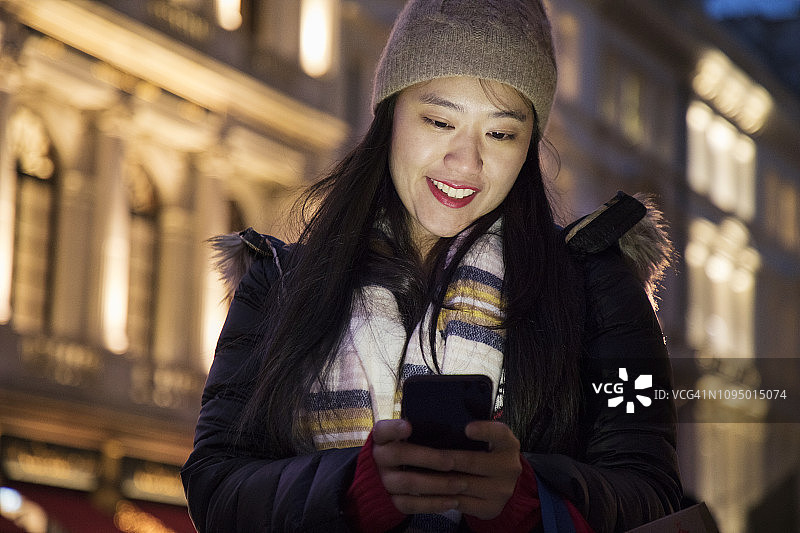夜晚站在城市街道上看手机的亚洲女性图片素材