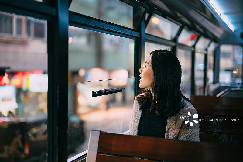 年轻女子在香港乘坐有轨电车欣赏城市夜景图片素材