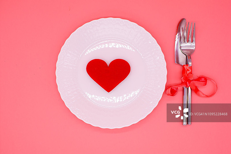情人节节日餐桌布置，粉色桌子上有餐具、兰花、礼品盒和红心，留有文字空间图片素材