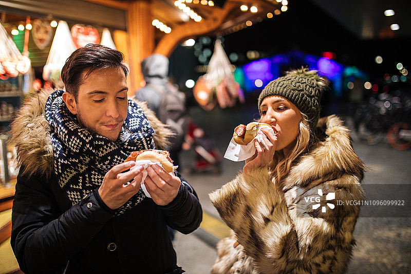情侣在圣诞市场前吃热狗图片素材