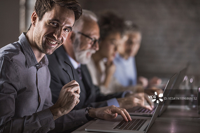 快乐的商人在办公室里用笔记本电脑工作图片素材