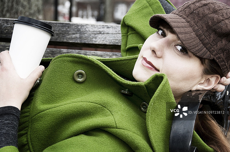 年轻女子坐在公园长椅上喝咖啡图片素材