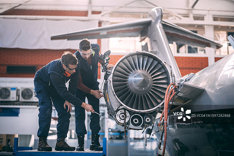 两名飞机机械师正在修理一架小型飞机的未覆盖的喷气发动机图片素材