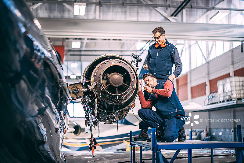 两名飞机机械师正在修理一架小型飞机的未覆盖的喷气发动机图片素材