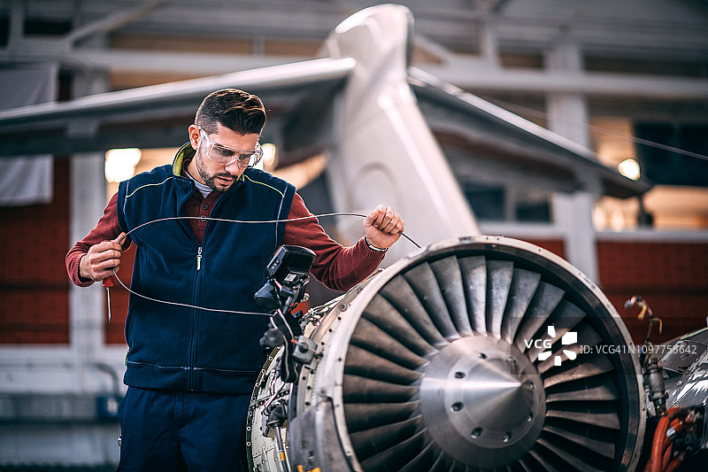 飞机机械师在维护机库中用便携式相机探测飞机的开放式喷气发动机并查看监视器图片素材