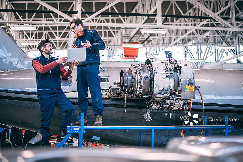 飞机机械师在机库中用笔记本电脑修理喷气发动机图片素材