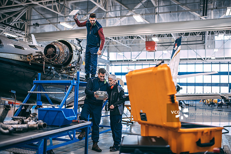 年长的女工程师在飞机维修库中，与她的团队一起检查小型私人飞机旁的诊断设备图片素材