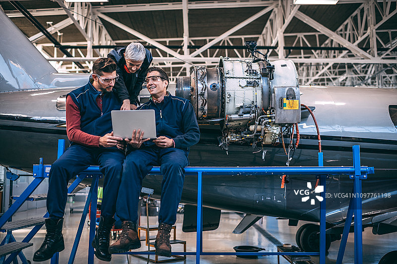 年长的灰发女工程师与男同事在飞机维修库中用笔记本电脑工作图片素材