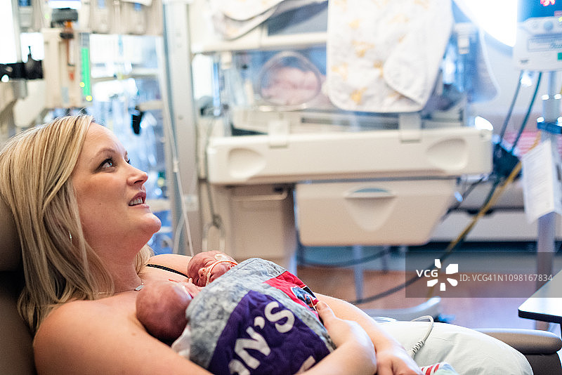 在新生儿重症监护病房，29周早产双胞胎与母亲在医院里进行肌肤接触，背景为暖箱图片素材