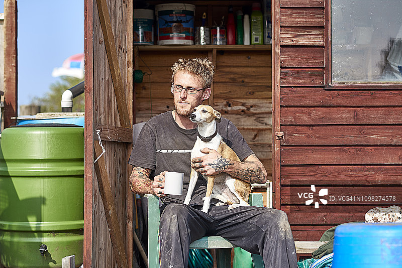 30多岁的英国男子坐在他的菜园里和他的宠物狗一起享受时光图片素材