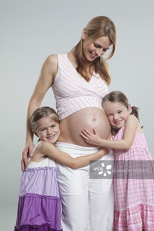女儿们拥抱怀孕的母亲，面带微笑图片素材