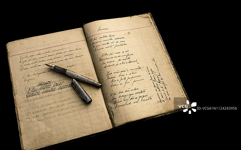 打开的旧书法笔记本，展示了笔迹演变，一支旧银笔放在上面，静物图片素材
