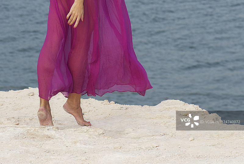 穿着长裙的女人站在沙滩上的腿部特写图片素材