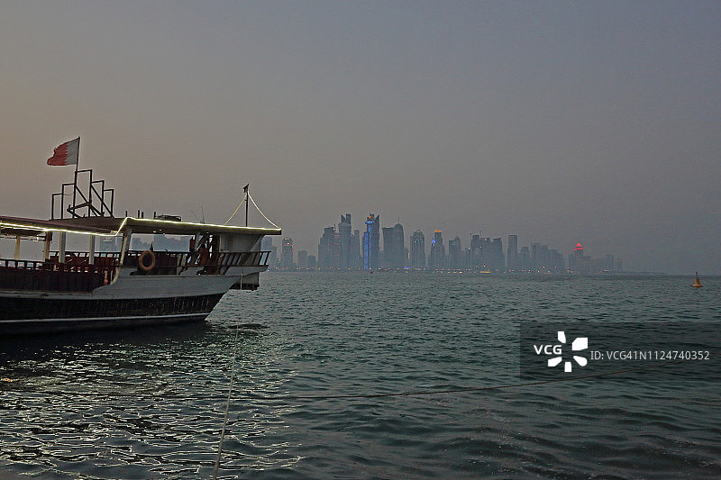 卡塔尔多哈，黄昏时分，停泊在滨海路对面的海湾中的三角帆船图片素材