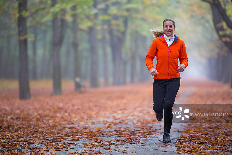 秋日清晨公园里独自跑步的快乐女人图片素材