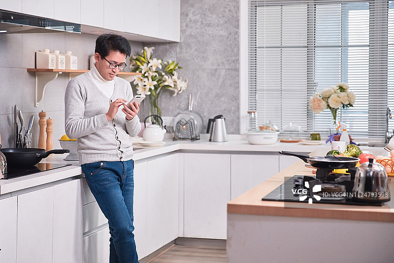 男人在厨房准备食物和发短信图片素材