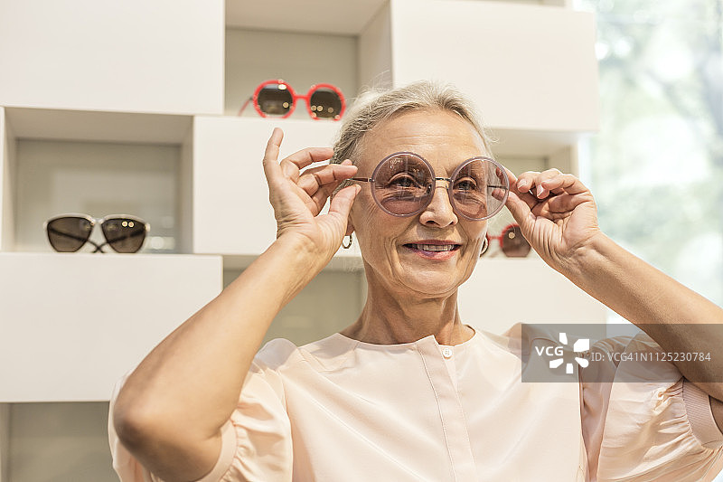 微笑老年女性在精品店试戴墨镜图片素材