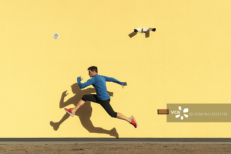 运动男士在黄色墙壁和监控摄像头旁锻炼图片素材