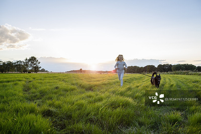 夕阳下，带着狗在田野上奔跑的女孩图片素材